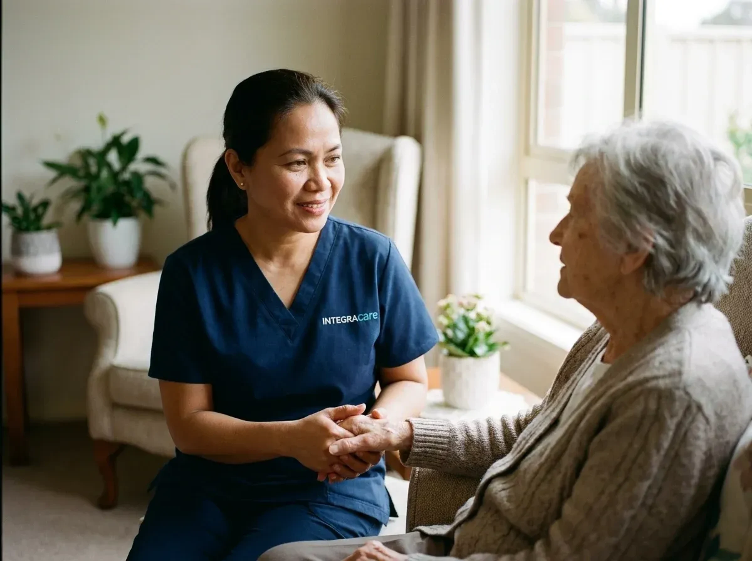 A caregiver sitting with an elderly woman at home, providing calm and attentive support