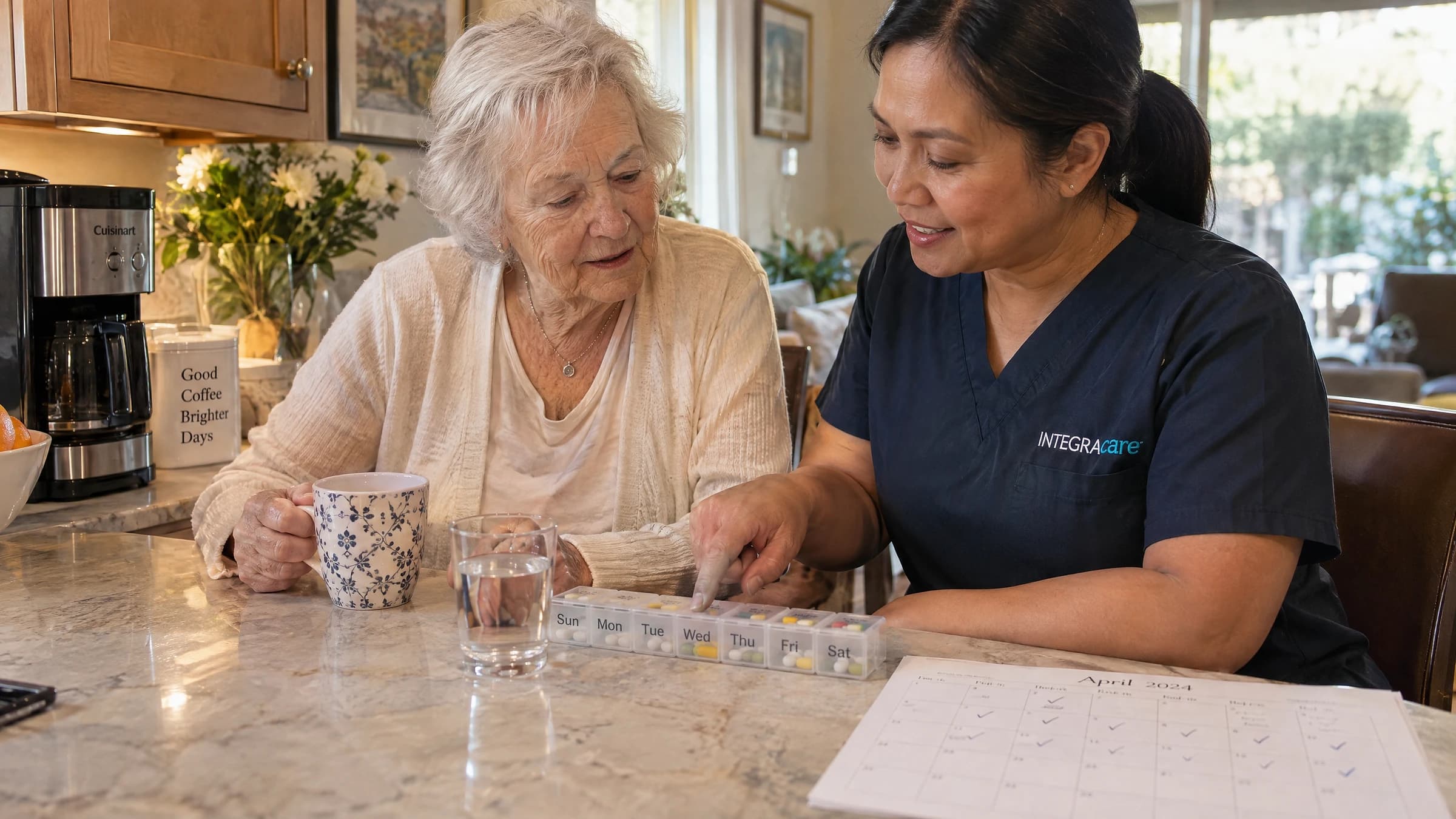 Caregiver helping a senior woman safely manage her morning medication using a blister pack and calendar at her kitchen table